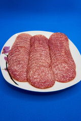 plate with salami slices on blue background