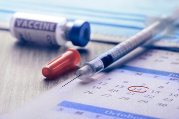 vaccination day, close-up of a syringe and vaccine with circled date in a calendar - 427589158
