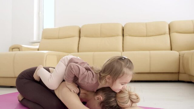 A little girl sits on her mother's back when she does yoga. Portrait