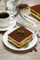 Traditional Italian Tiramisu dessert in glass baking dish and portion on grey concrete background