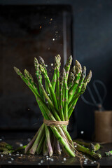 Fresh stems of green asparagus with spices around - salt crystals , dark wooden background. Macro view, copy space. Vegan, healthy eating, dieting concept. Organic vegetables.