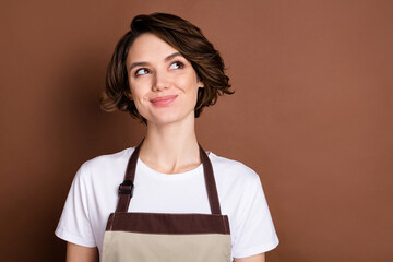 Photo of young smiling charming lovely woman barista look copyspace dreaming isolated on brown color background
