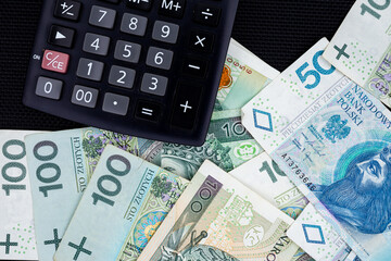 Calculator and Polish banknotes of PLN 100 and PLN 50 on a black background. Photo taken under soft artificial light