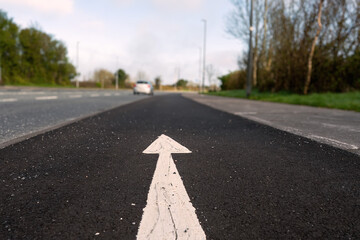 White arrow on a black asphalt surface in focus, moving car out of focus in th background....