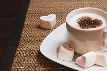 Cup of coffee with a heart made of chocolate chips with marshmallow hearts on a wooden table.