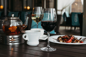 Fresh salad with vegetables and warm meat in white plate and glass of red wine on dark table on the summer terrace. Place for text.