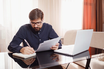 Entrepreneur works with a laptop and keeps a document in a home office
