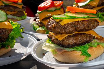 Tasty double cheeseburger with melted cheddar cheese dripping over ground beef burger garnished with fresh salad ingredients and served on a wooden table on an outdoor picnic table