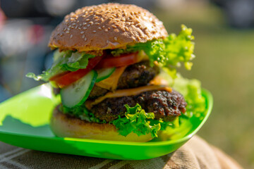 Tasty double cheeseburger with melted cheddar cheese dripping over ground beef burger garnished with fresh salad ingredients and served on a wooden table on an outdoor. Selective focus