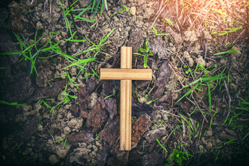 Wooden cross on the ground with bark and green grass.