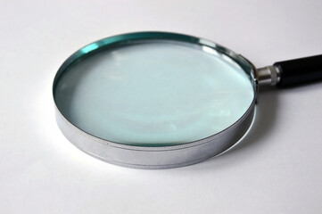 Magnifier with black handle on a white background. Part of the black handle is visible. Magnifying transparent glass. Fragment close-up