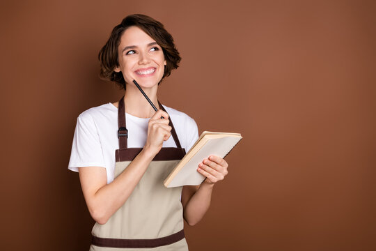 Portrait of pretty positive lady hold pen touch chin look interested empty space isolated on brown color background