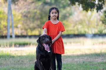 A young girl in red outfits plays with her big black dog in the backyard in the evening with her family