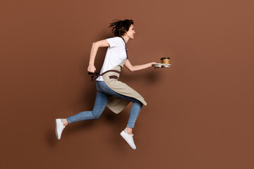 Fototapeta na wymiar Full size profile side photo of happy cheerful woman barista running with coffee look copyspace isolated on brown color background