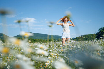 Pretty girl with a hat in her hand walks in a field with flowers and smiles sincerely. High quality photo.