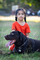 A young girl in red outfits plays with her big black dog in the backyard in the evening with her family