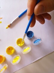 Hand with a brush, there are jars of paints of different colors next to it.