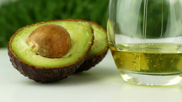 Pours avocado oil into a glass next to the avocado. 4K video close-up of healthy food.
