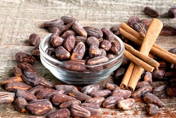 Cocoa beans in a glass bowl on a wooden background and sprinkled on the floor