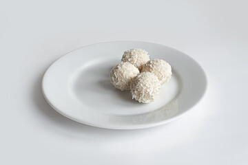 Sweet balls, white Chocolate candies with coconut crumb and white plate on white background. Handmade candies. Front view, mockup.