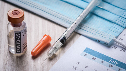 vaccination day, close-up of a syringe and vaccine with calendar on a table top - 427600754