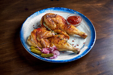 Georgian cuisine dish chicken tapaka or tabaka on a plate, on wooden background. Grilled chicken. close up