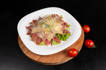 Beef carpaccio with rocket salad, parmesan cheese and lemon in a white plate isolated on black background. Top view, flat lay