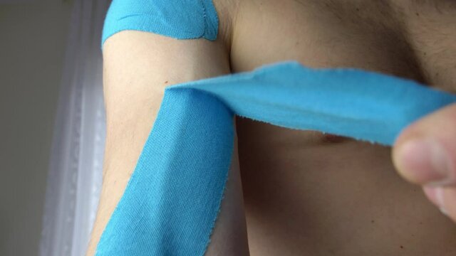 Taking off Kinesio Elastic Therapeutic Tape from Shoulder After Injury Treatment