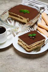 Traditional Italian Tiramisu dessert in glass baking dish, savoiardi cookies and portion on grey concrete background