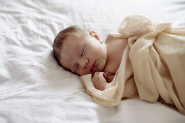 Little newborn baby sleeping on the bed in the bedroom, lulled by mom
