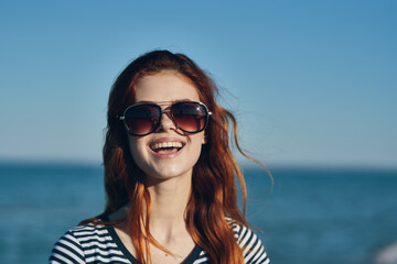 red-haired woman model in t-shirt and in sunglasses sea in the background summer vacation