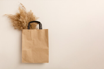bag from kraft paper with dry pampas grass on light-beige background. Natural eco-friendly style. Bouquet of pampas grass in a paper bag. Neutral colors background with copy space. Recycling materials