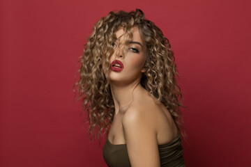 Sensual woman fashion model with curly hairstyle on red background