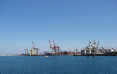 Fototapeta premium View from the sea station on the coastal cargo port surrounded by a calm surface of the blue sea.