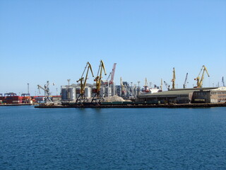 Fototapeta premium View from the sea station on the coastal cargo port surrounded by a calm surface of the blue sea.