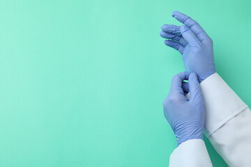 Doctor hands in medical gloves on mint background