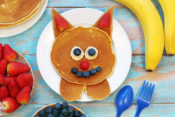 Fun food for kids. Cat shaped pancakes with berries on blue wooden table, top view. Healthy vegetarian food for children. 