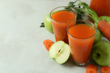 Glasses with juice and ingredients on white textured background