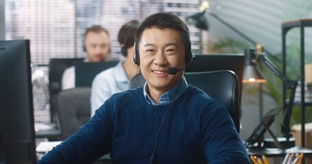 Close up portrait of Asian cheerful handsome male call center operator sitting at table at company...