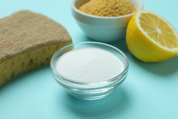 Bowls with mustard powder and acid powder, sponge and half of lemon on blue background