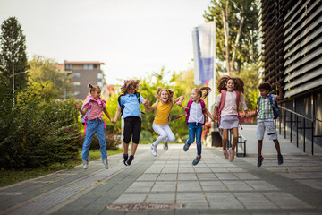 Group of elementary age schoolchildren jumping in schoolyard.