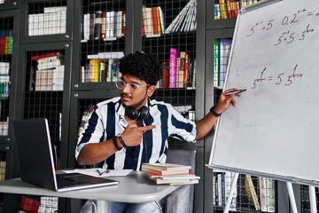 An Indian teacher during an online lecture, lessons, he points to the board with the solution of an example in mathematics and speaks to the computer