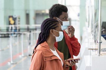 Safe travel and tourism during coronavirus outbreak: closeup of black couple in masks at airport check-in for flight. African male and female at terminal counter with passports in corona new normality