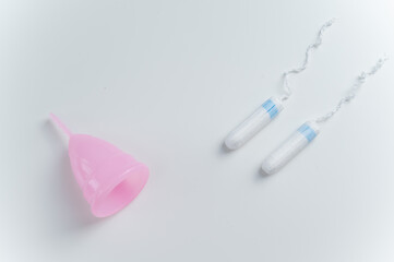 Pink menstrual cup and tampons on a white background. Comparison of personal hygiene products for women during menstruation