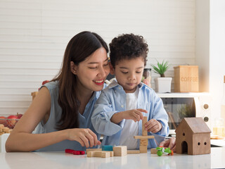 Pretty Asian mother playing with wooden blocks and house with cute mixed race son in the kitchen at home.