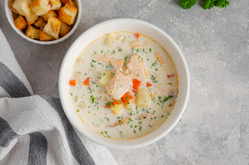Salmon soup with cream, potatoes, carrots, herb and croutons in a bowl on a gray concrete...