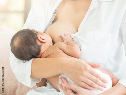 Breastfeeding, young Asian mom nursing her baby. Mother breast feeding new born child at home.