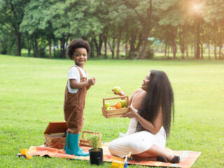 Dark skinned mother and son picnic in the park. Happy mom giving fruit to cute boy.