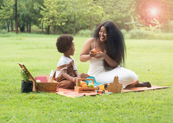 Dark skinned Mom and son spending quality time picnic in the park. Mother asking boy to eat fruit.  Bonding time and healthy food.