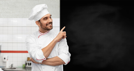 cooking, culinary and people concept - happy smiling male chef in toque with big black chalkboard white board over restaurant kitchen background